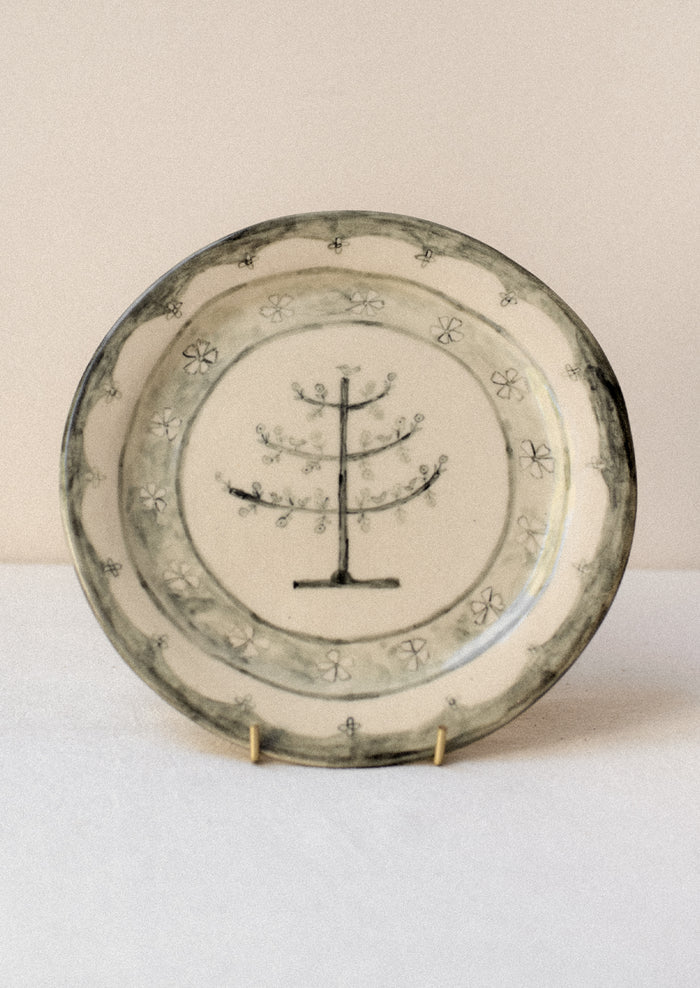 A cream ceramic plate with illustrated tree and flowers in dark grey.