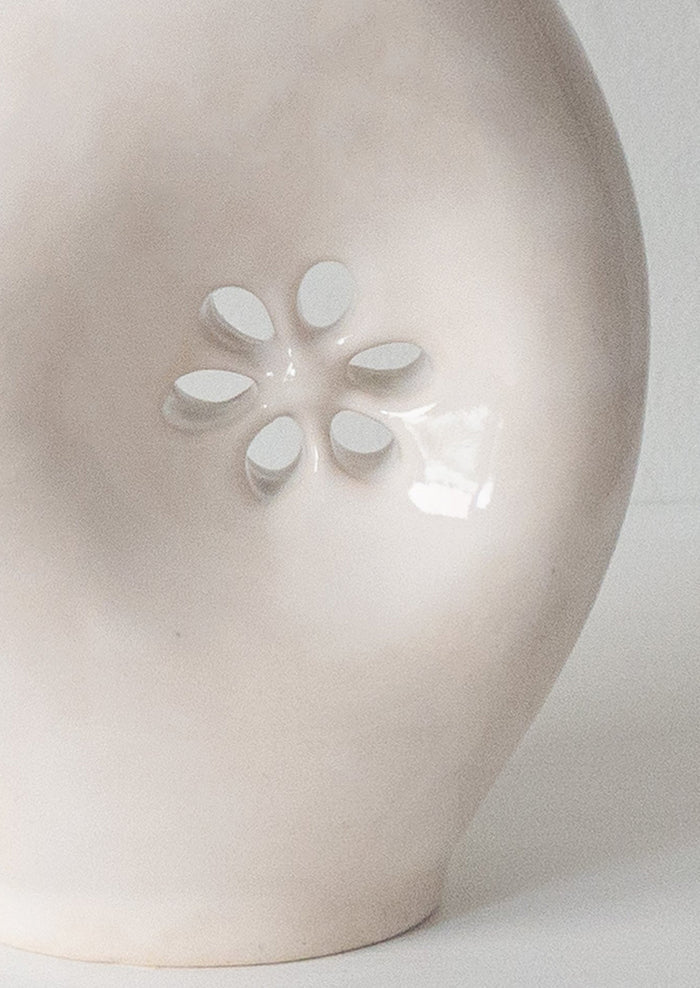 A glossy white ceramic vase with asymmetrical flower cutout detail.