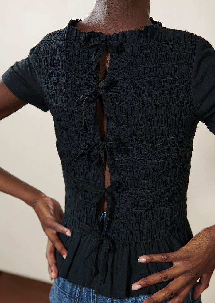 A woman wearing a smocked black short sleeve top with ties in back.