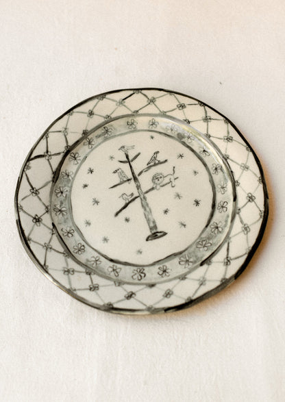 A cream ceramic plate with drawing of animals in tree and floral border in dark grey.