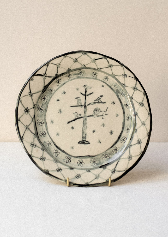 A cream ceramic plate with drawing of animals in tree and floral border in dark grey.