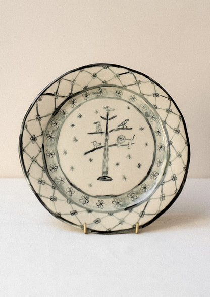 A cream ceramic plate with drawing of animals in tree and floral border in dark grey.