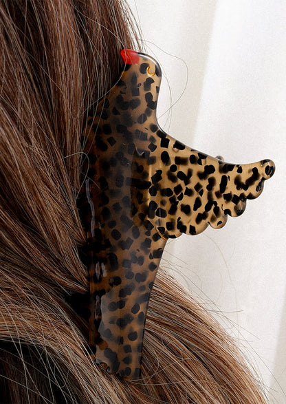 A person wearing a hair claw of brown bird with black spots and red beak.