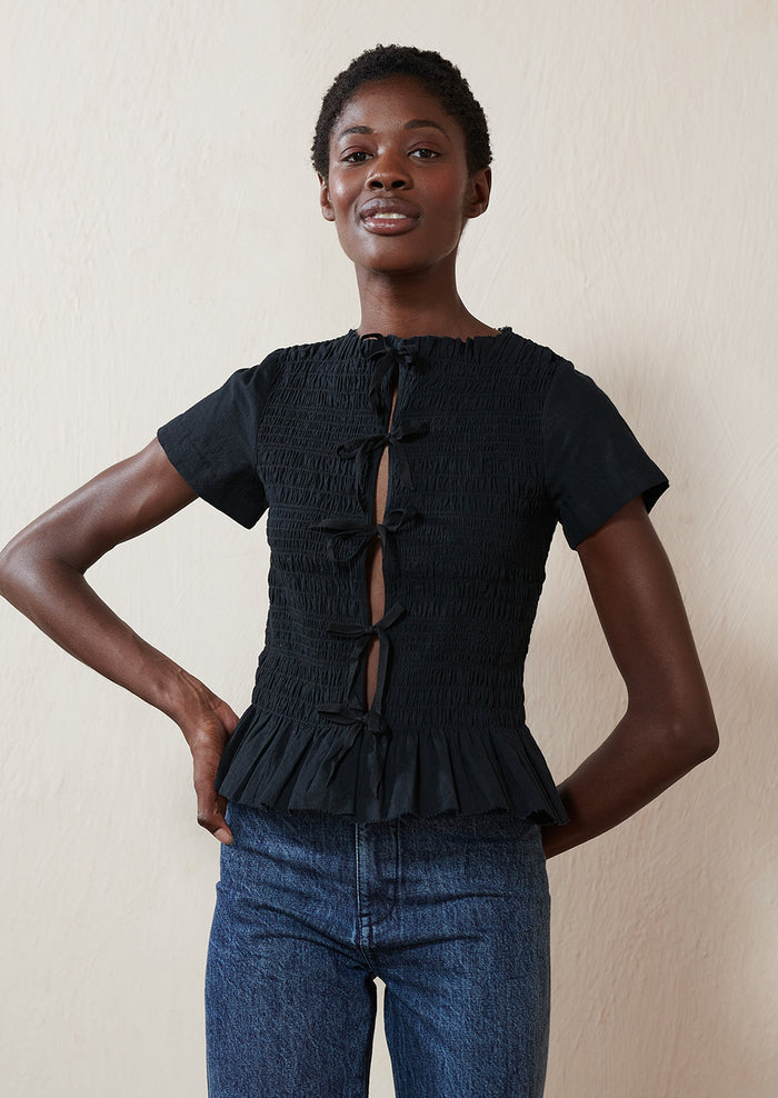 A woman wearing a smocked black short sleeve top with ties in front.