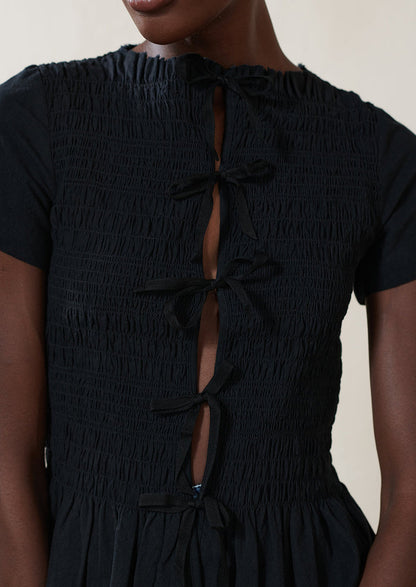 A woman wearing a smocked black short sleeve top with ties in front.