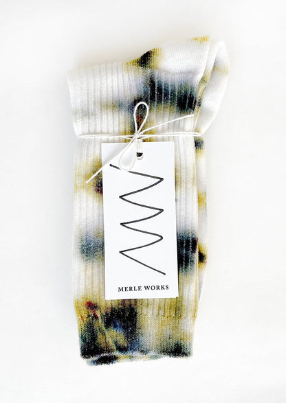 A pair of tie dye socks in white with mossy green and blue.