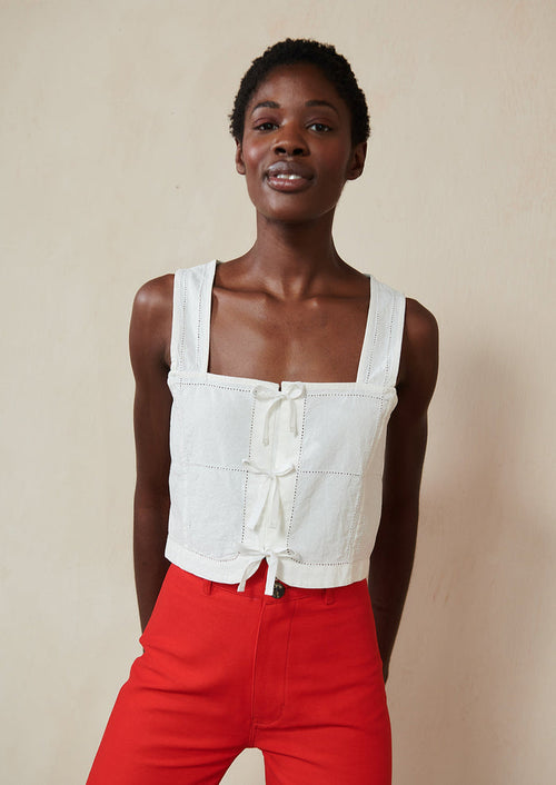 A woman wearing a white square neck tank with ties at front.