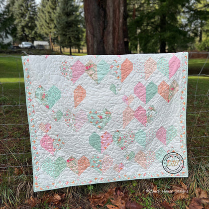 Lap quilt with two sizes of heart blocks using  a different fabric for  each side of the heart.  Quilt is made using a Layer Cake and is shown draped over a fence.