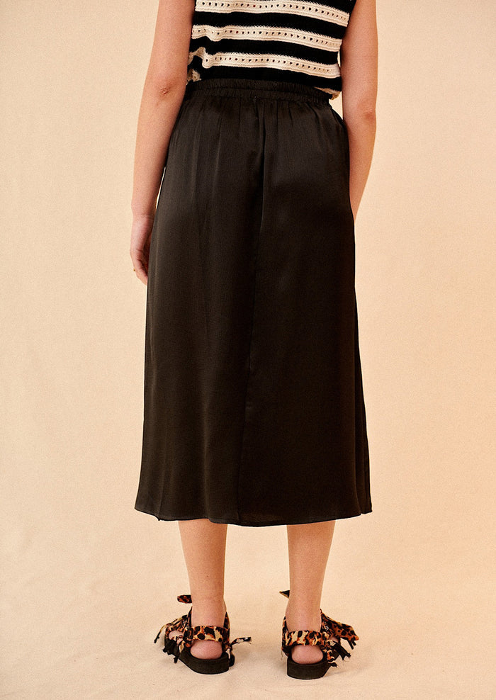 Woman wearing black midi skirt and sandals, seen from behind.