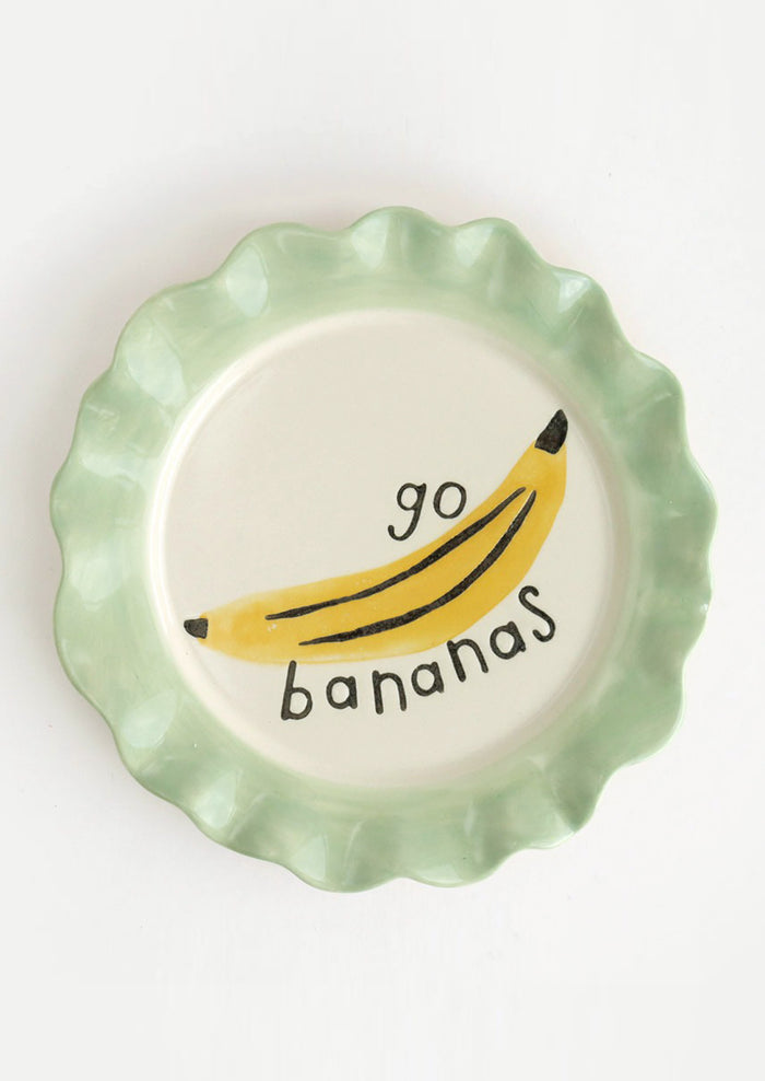 A printed ceramic plate with mint colored rim and banana graphic, text reads "Go bananas".
