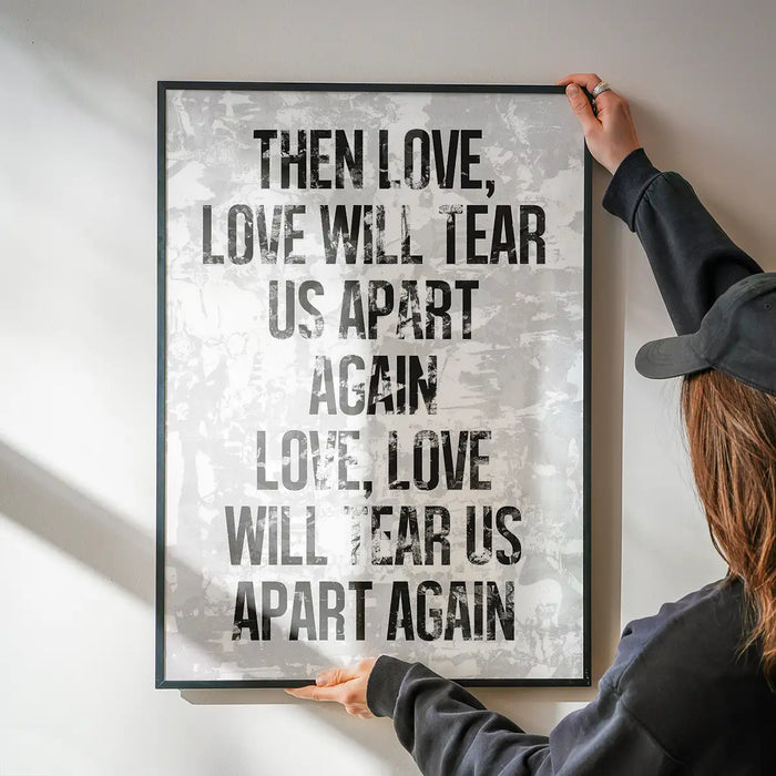 White grunge print with "Love Will Tear Us Apart" lyrics in bold black text, held by hands.