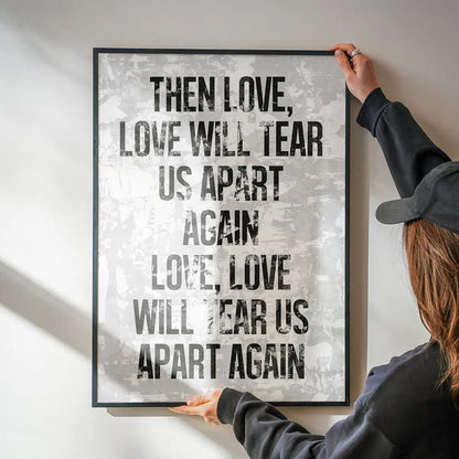 White grunge print with "Love Will Tear Us Apart" lyrics in bold black text, held by hands.