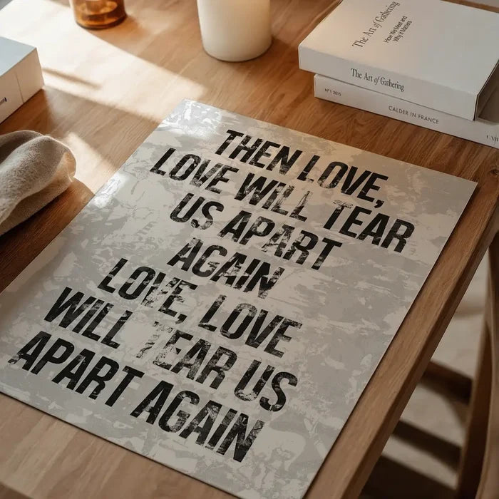 White grunge print art paper with "Love Will Tear Us Apart" lyrics in bold black text on a wooden table.