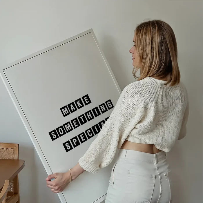 Woman holding a large white framed typographic print with "MAKE SOMETHING SPECIAL" in black block letters.