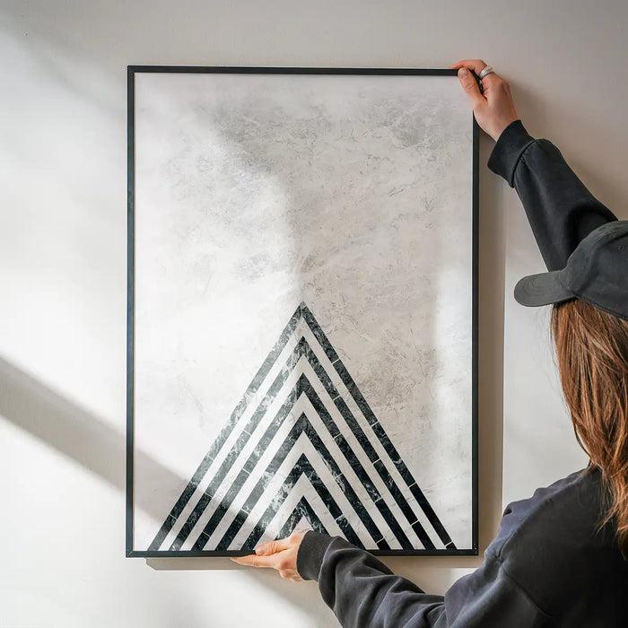 Abstract dark marble point art print with black frame, held by hands against a white wall.