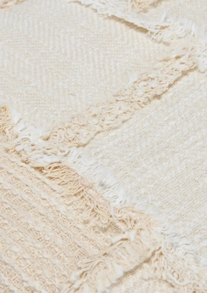 A throw pillow in natural cotton with patchwork detailing in different textures.