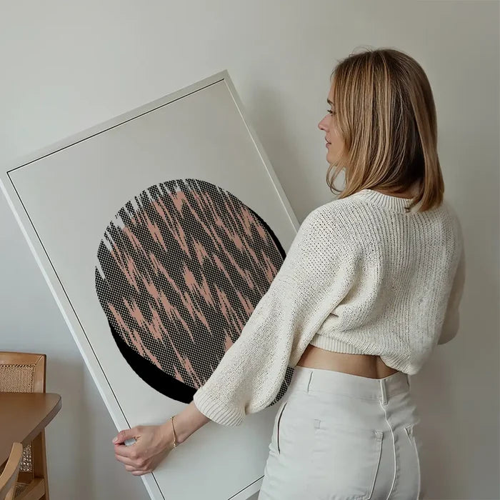 Woman holding a framed Pebble 1 abstract art print with a black and peach patterned circle.