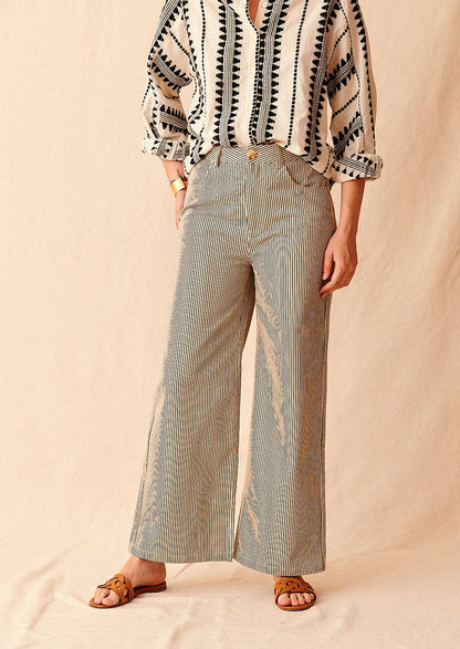 A woman standing wearing cream and black pinstriped wide leg jeans with brown sandals and cream and black embroidered top