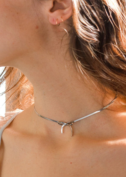 A woman wearing a silver choker-style necklace with bow shape at front.