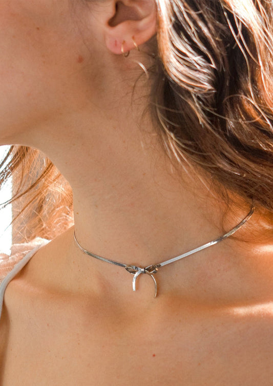A woman wearing a silver choker-style necklace with bow shape at front.
